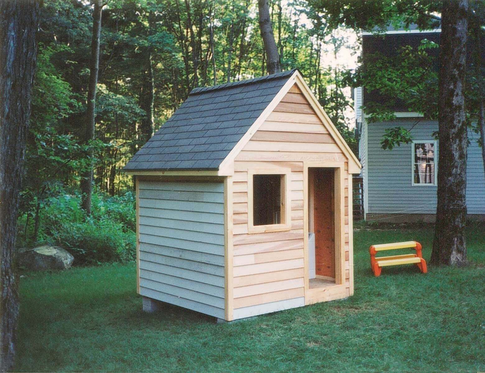 Children's playhouse with real wood siding and shingled roof. Open door and window.