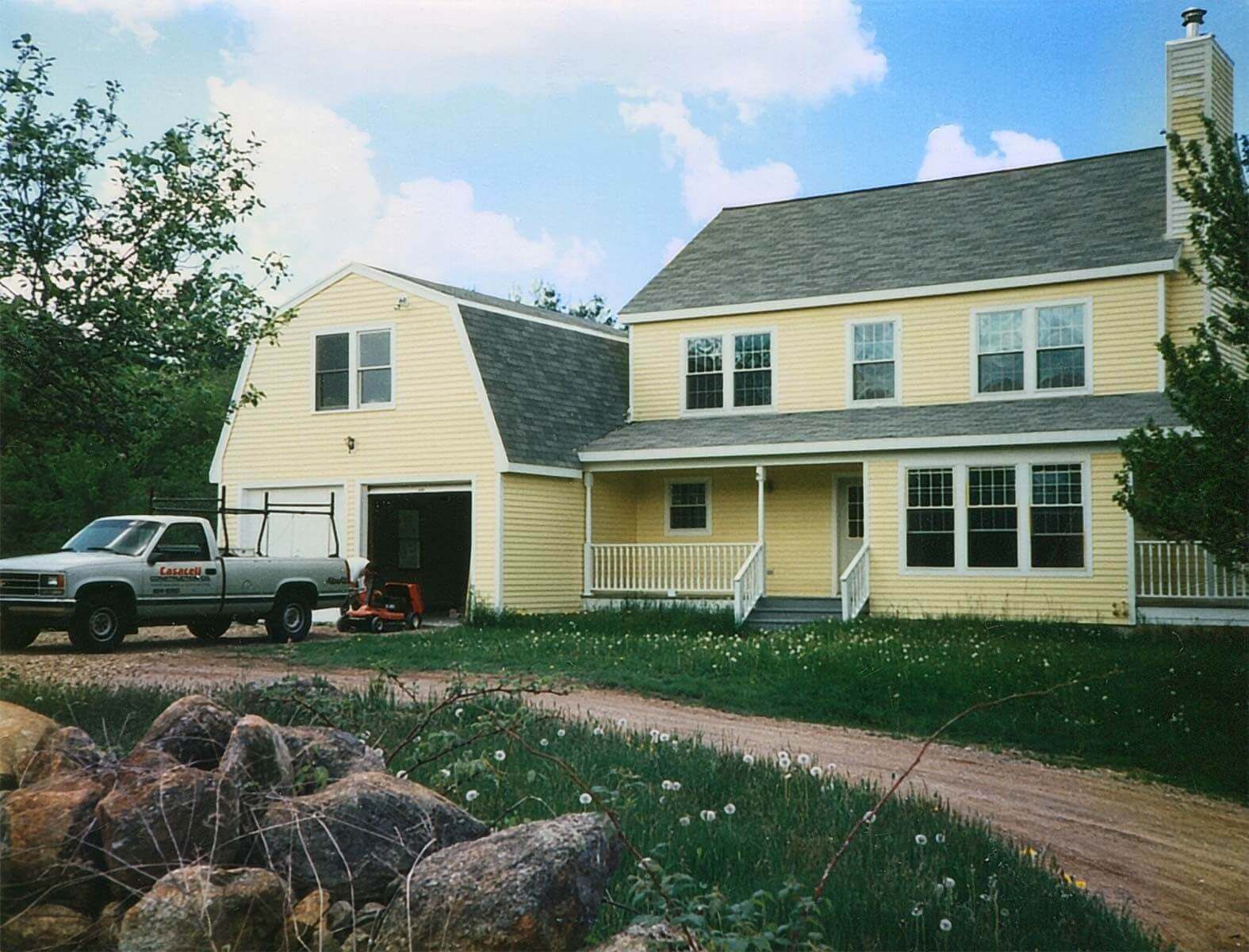 Two-story home with yellow siding and two front porches. Two car garage with second level storage and windows.